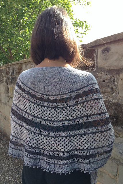 Person wearing a patterned shawl outdoors near a stone wall.
