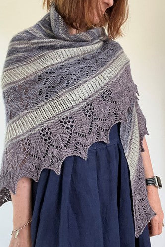 Person wearing a large, patterned knitted shawl over a dark blue dress against a plain background