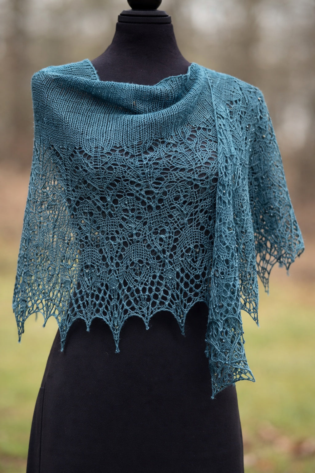 Teal knitted shawl on a mannequin against a blurred natural background