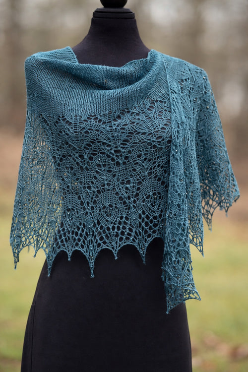 Teal knitted shawl on a mannequin against a blurred natural background