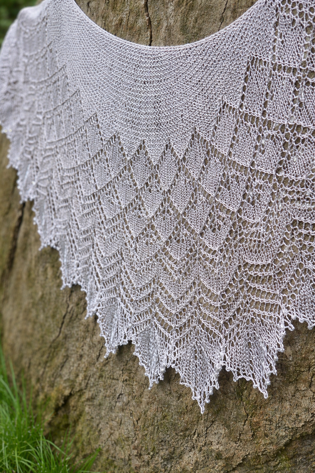 Knitted shawl with a lace pattern draped over a tree trunk.
