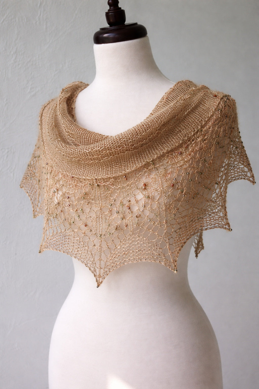 Knitted beige shawl on a mannequin against a plain background